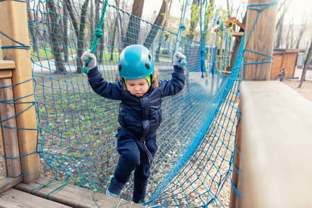 Portrait happy brave courage little toddler child boy wear safety equipment helmet enjoy passing obstacle course forest rope adventure park on cold winter day. Active outside leisure amusement campの写真素材