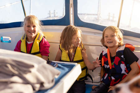 Portrait three little happy excited smiling caucasian children friends wear lifevest enjoy sailing...