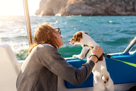Back view young adult caucasian woman enjoy petting cute adorable little jack russel dog sailing family luxury yacht boat against blue water bright sunny summer day. Travel sea tourism with pets.の写真素材