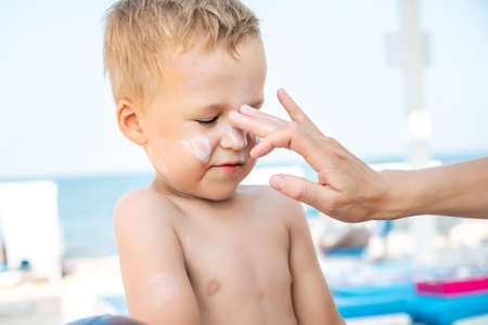 Mother applying sunscreen protection creme on cute little baby boy kid face. Mum using sunblocking lotion to protect son from sun during summer sea vacation. Child healthcare travel vacation timeの写真素材