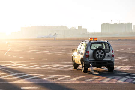 Scenic view of airport security car on tarmac apron taxiway in warm sunlight of bright morning sunrise or evening sunset time. Follow me safety vehicle staff. Aviation maintenance and service machineの写真素材