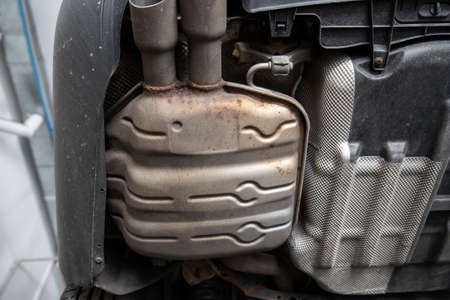 Close-up detail bottom view of car part metal exhaust muffler pipe with rusty stains. Lifted vehicle check-up maintenace service, repair and fix at automotive workshopの写真素材