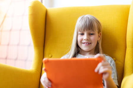 Portrait of cute adorable blond little kid girl enjoy sitting in cozy soft yellow armchair playing...