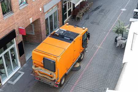 Top above view of small sweeping vacuum cleaner machine equipment removing dust rubbish city street sidewalk paved road near apartment condo building. Special municipal sweeper vehicle cleaning townの写真素材