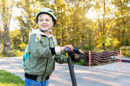 Profile view portrait of cute blond little caucasian school girl wear helmet enjoy having fun riding electric scooter city street park outdoors on sunny day. Healthy sport children activities outsideの写真素材