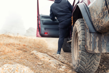 Bottom POV view male person driver open door of 4x4 awd suv vehicle on dirt gravel unpaved road in autumn at misty mountain top. Off road car mountain safari adventure nature trial journey conceptの写真素材