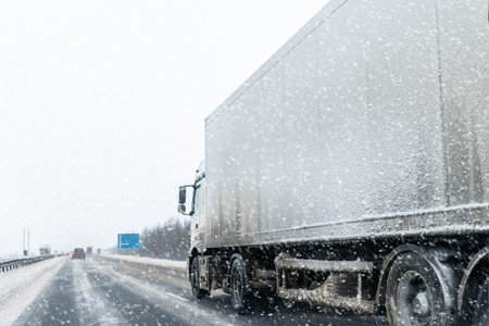 White blank modern delivery big shipment cargo commercial semi trailer truck moving fast on motorway road at heavy snowfall in winter. Business distribution logistics service. Lorry driving highwayの写真素材