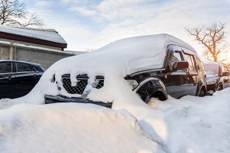 City street driveway parking lot spot with small car covered snow stuck trapped after heavy blizzard snowfall winter day by big snowy pile. Snowdrifts and freezed vehicles. Extreme weather conditionsの写真素材