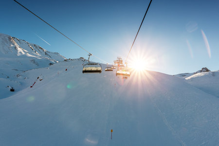 Ski lift empty ropeway on hilghland alpine mountain winter resort on bright sunny evening . Ski...