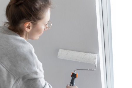 Close-up view young adult woman hand painting wall paint holding roller brush white color living room moving new home flat . Female painter decorating interior renovation residential apartmentの写真素材