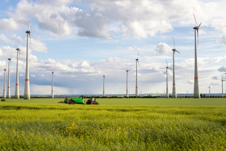 Scenic landscape view big modern tractor machine with sprayer equipment spraying fertilizer in rapeseed agricultural field against windfarm power windmill. Arable land cultivation sustainable energyの写真素材