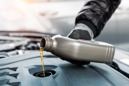 Close-up driver hand holding small bottle can pouring synthetic motor oil in diesel or petrol turbocharged vehicle engine due oil consumption. New lubricant diy change. Car service maintenance workの写真素材