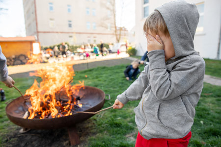 Cute little adorable baby boy put big wooden stick in fire pit with huge fire at house garden yard. Child play dangerous game with bonfire. Fire accident risk and health damgae conceptの写真素材