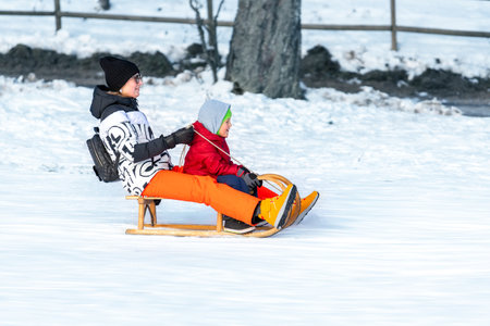Young adult mother with cute baby boy son enjoy have fun sledging downhilll at frozen white snow...