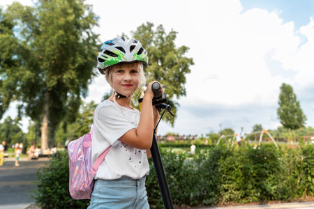 Profile view portrait of cute blond little caucasian school girl wear helmet enjoy having fun riding electric scooter city street park outdoors on sunny day. Healthy sport children activities outsideの写真素材