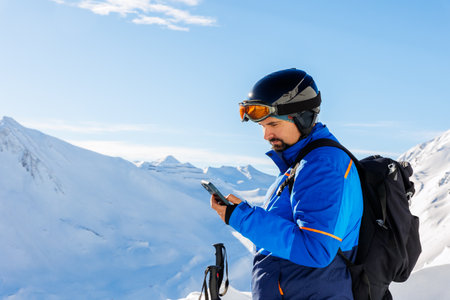 Young adult skier use smartphone make selfie navigate online map app winter alpine skiing resort. Male sporty person with backpack using mobile phone mountain Alps snow slope outdoors cold snowy dayの写真素材