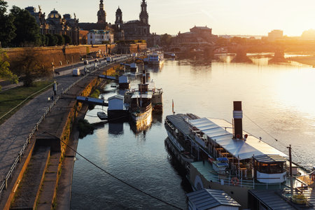 Scenic warm sunset beautiful Dresden city skyline at Elbe River with many steam tourist ship vessel moored at bank. Saxony Germany capital cityscape dusk panoramic view with old Europe architectureの写真素材