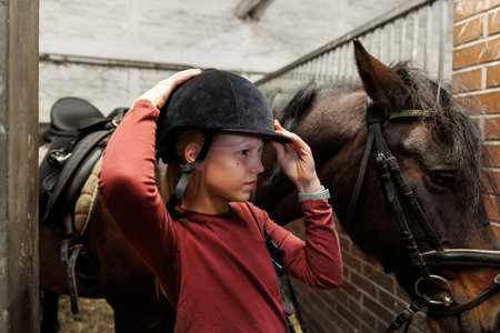 Young little teenager kid girl cleaning grooming chestnut horse back hair brush tool horse at stable ranch. Horse ride school farm life. Cute little blond girl kid care brown horse. Equine hobby workの写真素材
