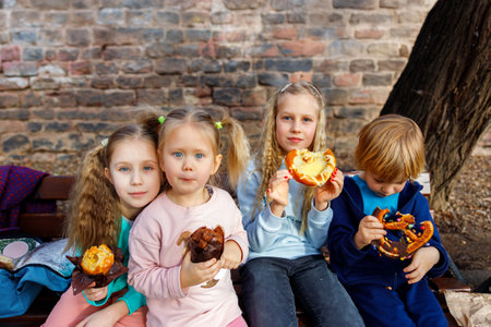 Portrait group happy funny playful blond children enjoy eating pretzels chocolate toppings at city...
