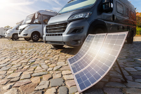 Many modern parked camper vans charge battery generator portable solar panels by clean eco energy, enabling off-grid travel freedom travel on sunny summer day. Innovative sustainability technologyの写真素材