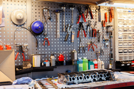 Pegboard wall with pliers, wrenches and handtools overlooks workbench holding engine block, coolant and oil cans. Industrial workshop scene highlights mechanical precision and automotive repair skillの写真素材