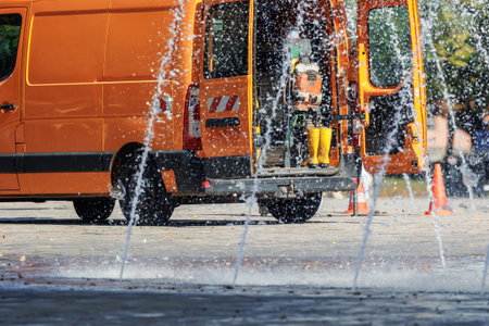 Orange utility service van doors open parked near working fountain in city street center. Fountain system maintenance, inspection winterization work. Equipment tools water accident emergency vehicleの写真素材