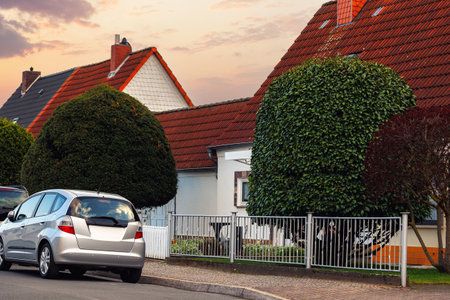 City street single-family modern houses Germany against warm sunset sky. German suburban small town residential area row eco sustainable life building neighborhood suburb. Urban car parking drivewayの写真素材