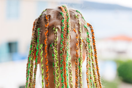 Back view cute blonde girl with colorful braided hair on sunny day seaside beach coast vacation. She...