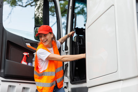 Portrait young adult happy smiling laughing woman climbing cabin heavy truck driver cargo vehicle. Female person girl professional job career working driving freight engine lorry. Logistics industryの写真素材