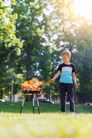 Cute little adorable baby boy put wooden stick in fire pit with huge fire at city park or house yard. Child play dangerous game with bonfire. Fire accident risk and health damage conceptの写真素材