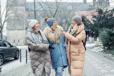 Three cheerful young adult women friend walk Magdeburg street old european uk german town city street enjoy having fun laughing cold winter day together. Female persons friendship celebration weekendの写真素材