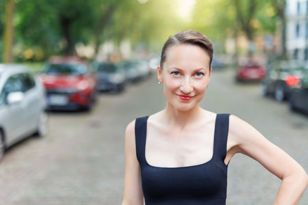 Confident pretty young adult woman portrait in black dress smiling playful expression while standing on city street. Elegant and stylish look. Female person walking city roadの写真素材