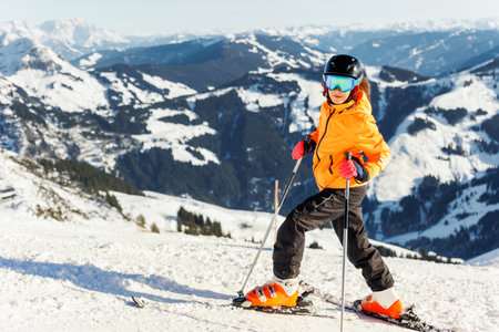 Active confident adorable teenager caucasian kid girl portrait with ski in helmet, goggles and bright suit enjoy winter extreme sport activities. Little child skiing luxury alpine resort in mountainsの写真素材