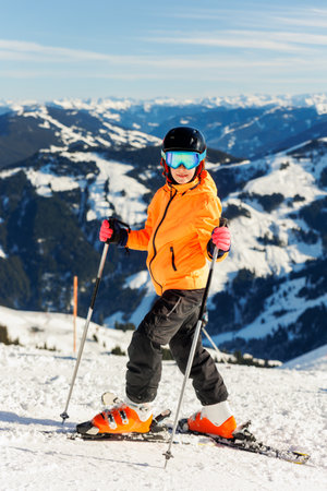 Active confident adorable teenager caucasian kid girl portrait with ski in helmet, goggles and bright suit enjoy winter extreme sport activities. Little child skiing luxury alpine resort in mountainsの写真素材