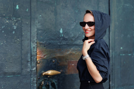 Portrait young adult elegant woman black dress and sunglasses smiles confidently in golden sunlight warm sunset backlit light against historic cathedral building. Female person walking city streetの写真素材