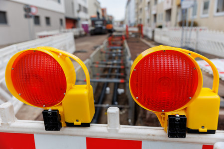 Urban street excavation with visible pipelines and safety barriers. Red warning lights and...