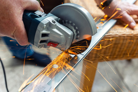 A person is cutting metal with an angle grinder, producing bright orange sparks flying in different...