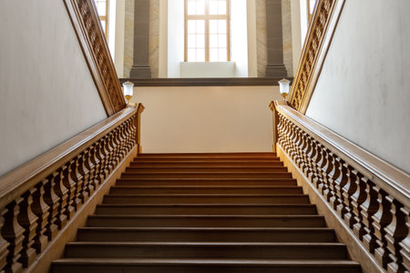 Elegant wooden vintage empty staircase rises toward large bright windows filled with warm light. Symmetrical balustrades and refined craftsmanship convey timeless elegance and architectural harmonyの写真素材