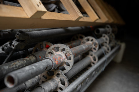Stack of metal scaffolding parts stored with wooden planks above creates industrial composition....