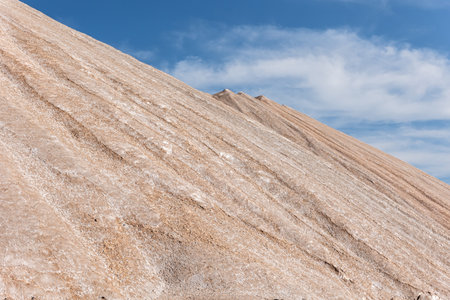 Potassium ore dump. Massive mound potash waste rises deep blue sky, its surface marked by mineral...