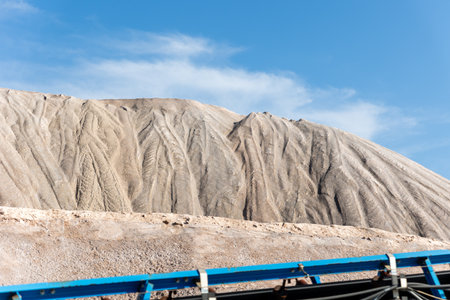 Long blue conveyor belt transports white potash ore material toward massive potassium mining dump...