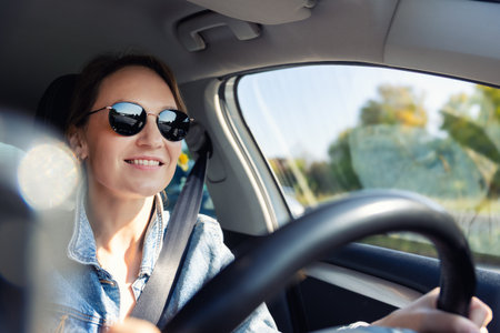Portrait young adult happy smiling woman in sunglasses drives sunny highway road wearing denim...