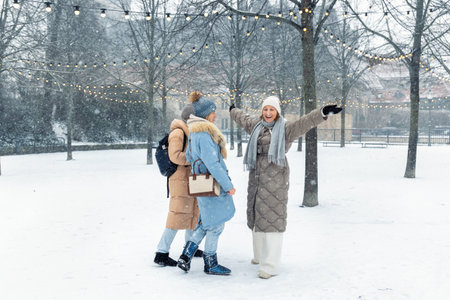 Group young adult smiling women wear long quilted coat white hat enjoy play snowball snowy day outdoors friends. Snowflakes fall playfully in front stairs decorated with glowing winter lightsの写真素材