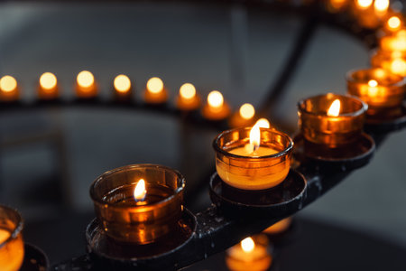 Burning votive candles warm glow in circular stand rack at french catholic cathedral church dark background. Prayer, hope, faith, remembrance prayer spirit in tranquil atmosphereの写真素材