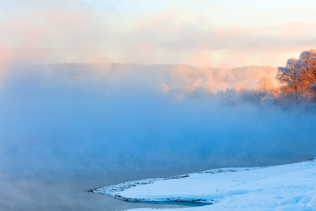 Winter landscape of trees and river in a foggy morning. Frost and cold and sunshine.の写真素材