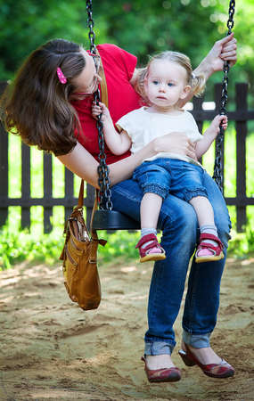 Full length of a happy mother and daughter sitting on swingの写真素材