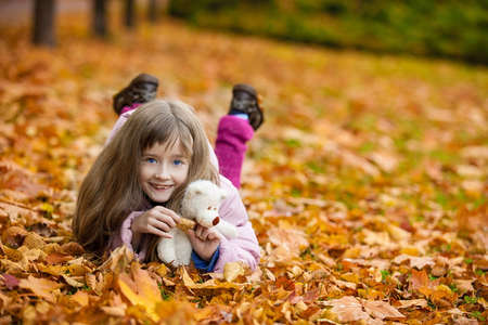 Portrait of little smiling girl in autumn lying on yellow leafsの写真素材