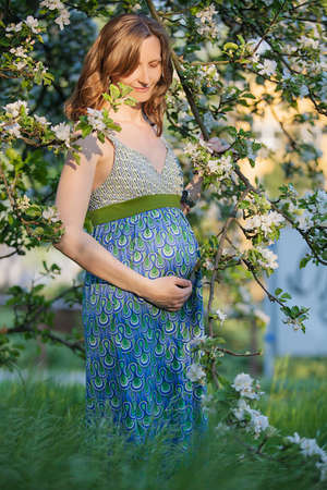 Portrait of beautiful pregnant woman in green dress in the flowering spring parkの写真素材