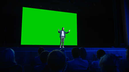 On Stage, Keynote Speaker Presents New Product to the Audience, Behind Him Movie Theater with Green Screen, Mock-up, Chroma Key. Business Live Event or Device Revealの写真素材