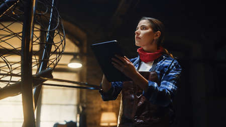 Beautiful Female Artist Sketches on a Tablet Computer Next to Brutal Metal Sculpture in Studio....